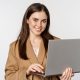 Portrait of corporate woman working with laptop, smiling and looking assertive, white background Portrait of corporate woman working with laptop, smiling and looking assertive, white background.